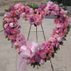 Heart-shaped pink and purple floral wreath on an easel with a ribbon bow