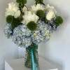 White roses and blue hydrangeas in a glass vase with green pom-pom accents