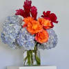 Bouquet of blue hydrangeas and orange-red flowers in a glass vase