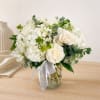 White roses and hydrangeas arranged in a glass vase with a ribbon