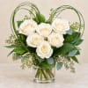 White roses arranged in a glass vase with looping green wire accents