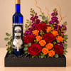 Red and orange roses with purple flowers arranged beside a decorated blue bottle