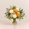 Bouquet of cream roses, orange pincushion blooms, and pink flowers in a glass vase