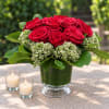 Red roses arranged in a green glass vase with two lit candles nearby
