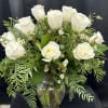 White roses arranged in a clear glass vase with mixed greenery