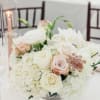 A low, rounded centerpiece built from clouds of white hydrangeas and blush-to-ivory