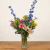 Mixed bouquet of blue, pink, yellow, and white flowers in a glass vase