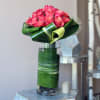 Pink roses arranged in a tall glass vase wrapped with green leaves