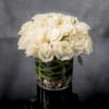 Compact arrangement of white roses in a clear glass cylinder vase with stones at the base