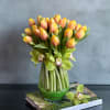 Peach and yellow tulips with green orchids in a clear glass vase set on two books