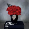 Compact arrangement of red roses with black fern accents in a faceted black vase on a book.