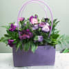 Purple and lavender flowers in a lavender handbag-style container with double handles