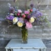 Tall mixed bouquet of pink, purple, and white flowers in a glass vase