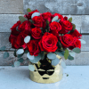 Red roses arranged in a gold vase with eucalyptus accents