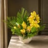 Yellow orchids arranged in a white bowl vase with palm fronds