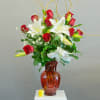 Red roses and white lilies in a red glass vase with a small yellow candle.