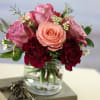 Pink and peach roses with burgundy carnations in a glass vase