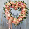 Heart-shaped floral wreath with pink roses and a satin ribbon on a stand