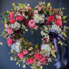 Heart-shaped floral wreath with pink, purple, and blue flowers on a dark stand