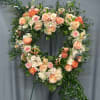 Heart-shaped floral wreath with peach and pink roses on a stand