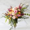 Large mixed bouquet of pink, peach, white, and yellow flowers in a clear glass vase