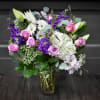 Bouquet of pink roses, white lilies, and purple flowers in a glass vase