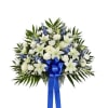 Standing spray of white lilies, roses, and carnations with blue flowers and a blue ribbon bow