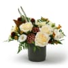 Low arrangement of cream roses, white blooms, and yellow accents in a dark cylinder vase with lotus pods.