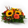 Low autumn centerpiece with bright yellow sunflowers, orange roses, red spray roses, and small pumpkins.