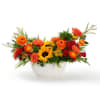 Low centerpiece with yellow sunflowers, orange roses, and red blooms in a white bowl.