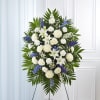 Standing spray of white lilies, roses, and mums with blue flowers on an easel