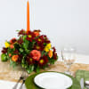 Autumn floral centerpiece with a tall orange candle on a table setting