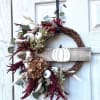 Fall wreath with dried flowers, eucalyptus, and white pumpkin accents on a wood door sign