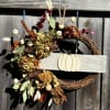 Fall wreath with dried flowers, pinecones, and a pumpkin sign on a wooden fence