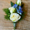 White rose boutonniere with blue flowers and greenery