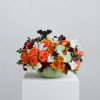 Orange roses and mixed flowers arranged in a pale green pumpkin vase with a bat topper.