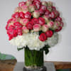 Pink and white roses arranged in a glass vase with white hydrangeas