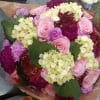 Bouquet of pink roses, hydrangeas, and burgundy flowers wrapped in paper