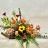 Mixed floral arrangement in a woven basket with bright orange, yellow, pink, and burgundy blooms