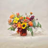 Mixed bouquet of orange, yellow, and purple flowers in a red glass vase