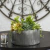 Succulent arrangement in a ribbed metal container beside a small candle holder
