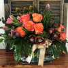 Mixed bouquet of orange roses, pink tulips, and dark orchids in a glass vase