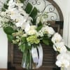 White orchid and rose arrangement in a glass vase with green accents