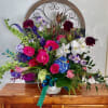 Colorful mixed flower arrangement in a white container with a teal ribbon