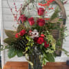 Red roses and berries arranged in a tall glass vase with holiday greenery