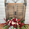 Red and white rose arrangement with holiday ornaments in a silver container