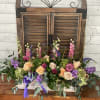 Low floral arrangement with roses, purple blooms, and greenery in a white container