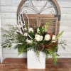 White roses in a white vase with pinecones and greenery