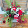 Red rose arrangement with pine, berries, and a striped ribbon in a rustic container