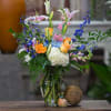 Mixed bouquet in a glass vase with orange roses, lilies, hydrangea, and blue flowers